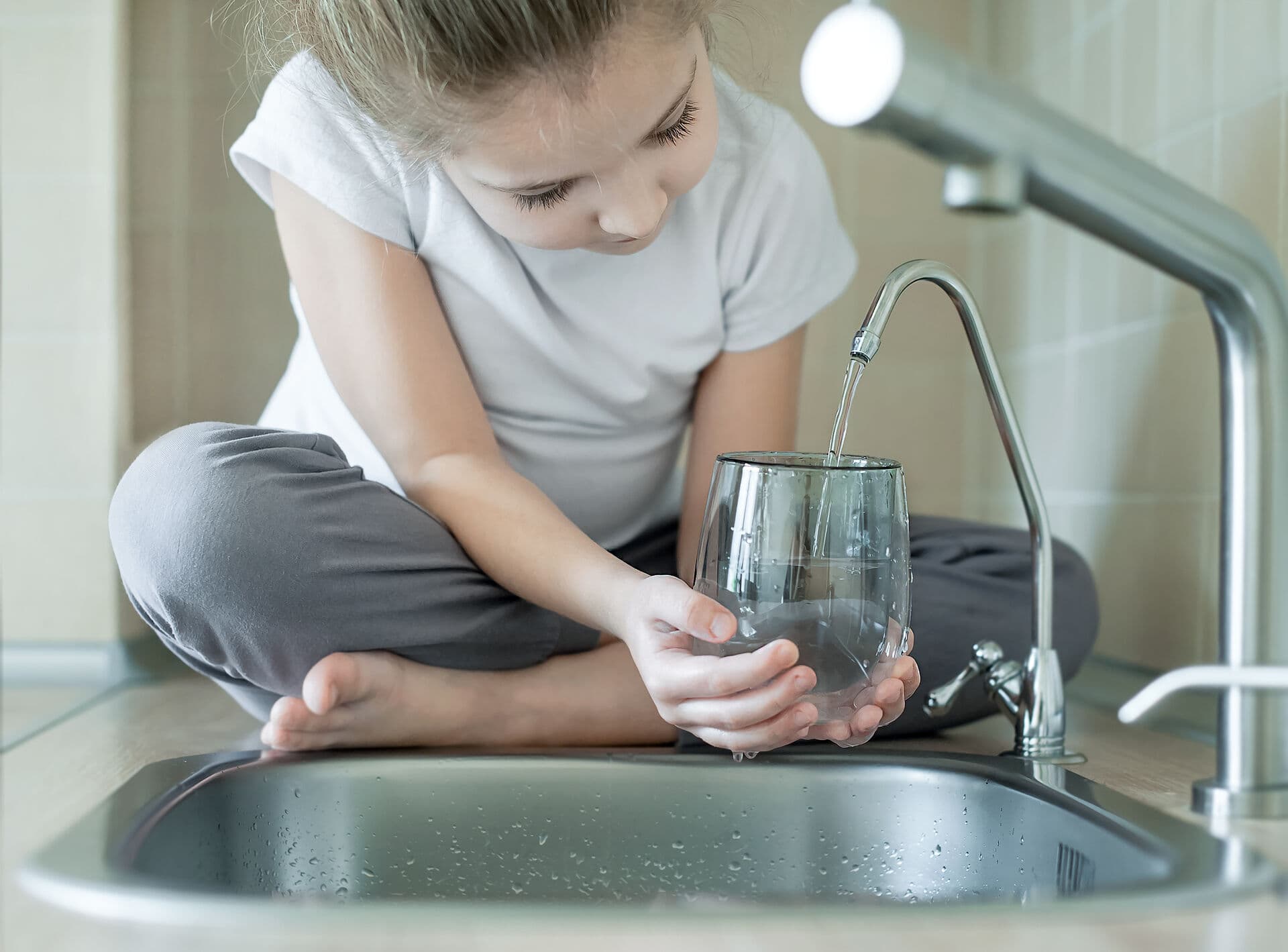 Child filling a glass of clean water from the kitchen faucet