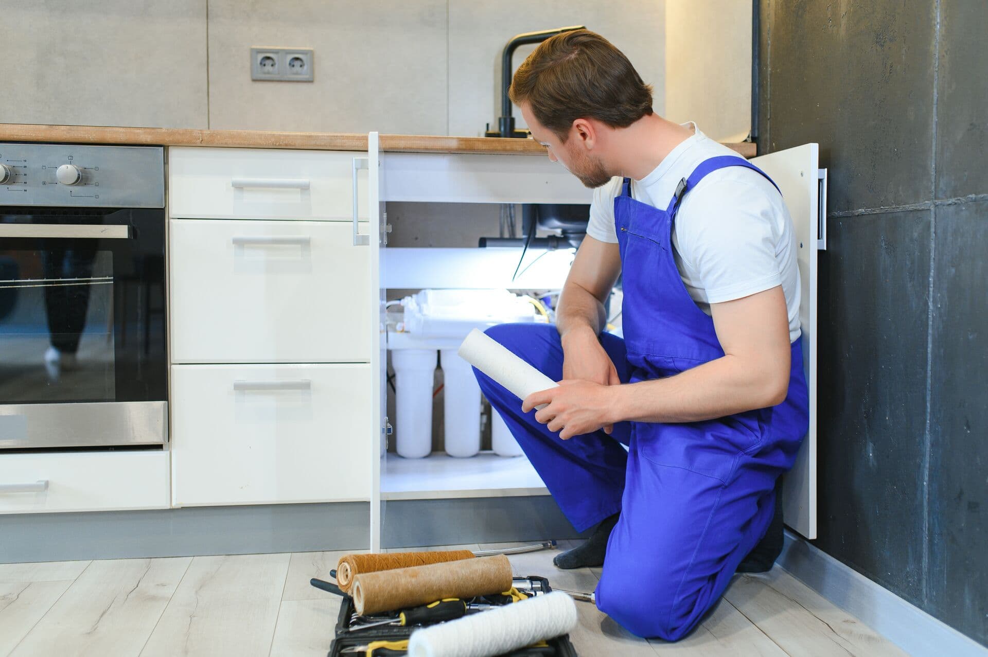 Technician replacing water filter under sink during emergency service call